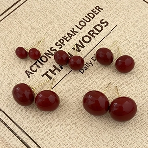 Close-up of glossy dark red spherical stud earrings in four sizes on a vintage card
