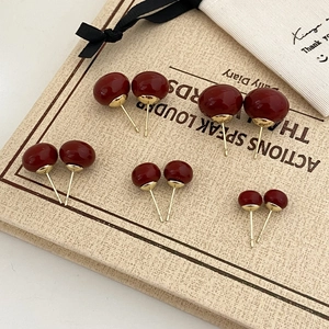 Close-up of five pairs of dark burgundy pearl stud earrings in various sizes on a notebook