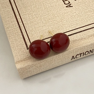 Macro detail of glossy dark red spherical stud earrings with gold pins on vintage book