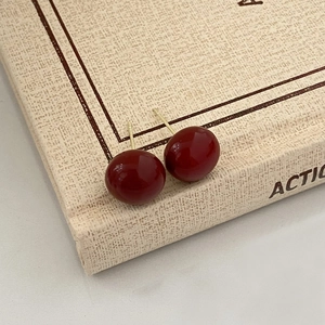 Detail view of retro wine red pearl stud earrings with smooth finish on a beige textured book