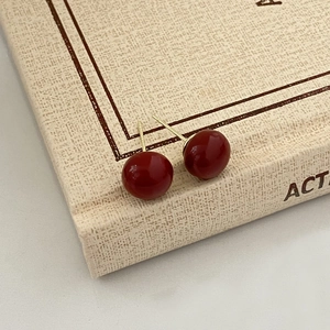 Macro shot of glossy red ball stud earrings on a textured vintage book cover background