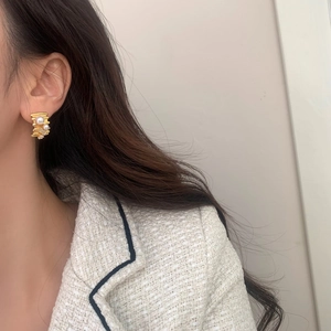 Close-up of C-shaped gold earrings with white pearls and sparkling zircons on model