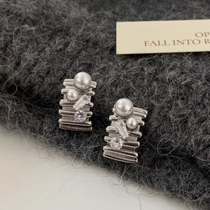 Macro detail of silver zircon pearl earrings on grey knit background showing fine texture