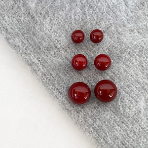Three pairs of vintage burgundy pearl stud earrings in varied sizes on a knit background