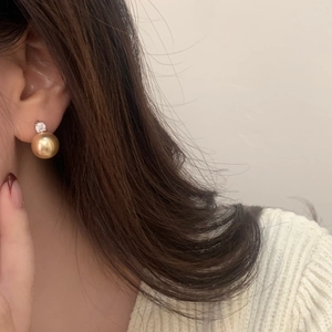 Close-up of elegant gold pearl earring with zircon stud worn on a model's ear