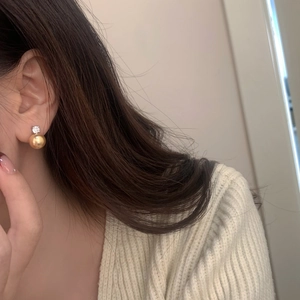 Close-up of elegant gold pearl earrings with sparkling zircon on a woman wearing knitwear