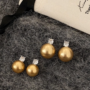 Detail of gold pearl earrings with white zircon accents in two sizes on grey fabric