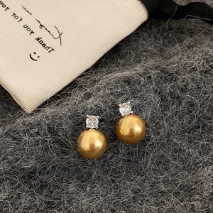 Macro view of gold-colored pearl earrings with zircon detail on grey wool fabric