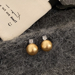 Macro detail of a 10mm golden pearl earring with a sparkling white zircon on grey felt