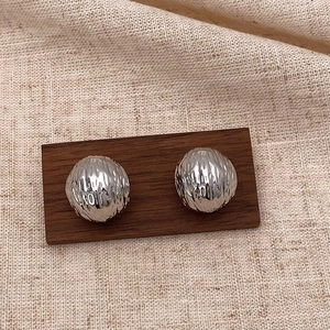Macro detail of silver C-shape earrings with hammered texture on a wooden display