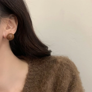 Close-up of caramel brown spherical stud earrings worn with a cozy knit sweater