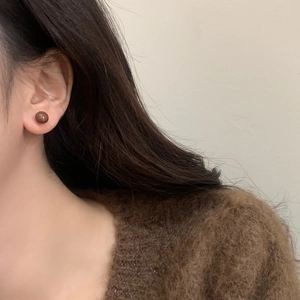 Close-up of a minimalist vintage brown enamel stud earring worn with a knitted sweater