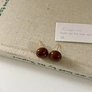 Close-up of deep brown spherical stud earrings with polished finish on a vintage book