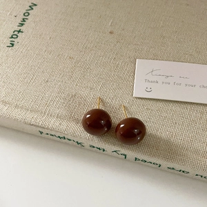 Detailed close-up of dark brown enamel ball earrings on a minimalist beige book background