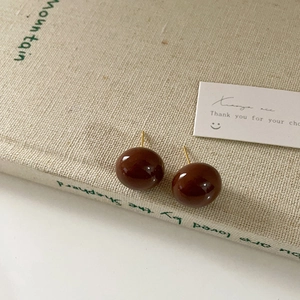 Detailed close-up of dark brown spherical enamel stud earrings on a beige fabric background