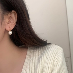 Detailed view of an elegant round pearl earring with gold hook on a model wearing white knit