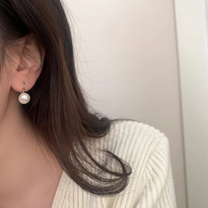 French style pearl drop earrings with silver hooks worn by a model in a cozy setting