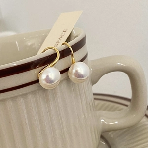 Detail of elegant pearl drop earrings hanging on a vintage ceramic cup with golden hooks