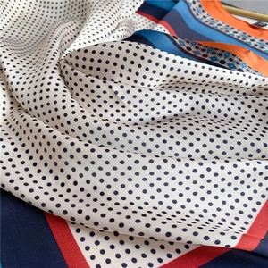 Gros plan d'un foulard en soie à pois noirs et bordures géométriques multicolores