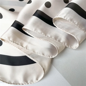 Close-up of silk-like satin scarf featuring black polka dots and hand-rolled edge detail