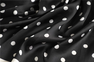 Macro detail of silk-like scarf fabric showing glossy black and white polka dot pattern
