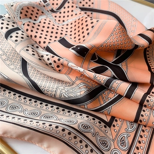 Gros plan d'un foulard en soie rose corail avec motif cachemire, pois et détails équestres