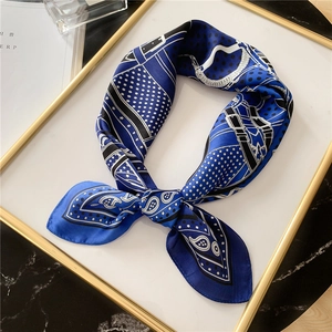 Détail d'un foulard en soie bleu roi aux motifs paisley et chaînes sur fond de marbre