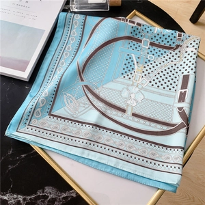 Détail d'un carré de soie bleu ciel avec motifs paisley et ceintures dans un plateau