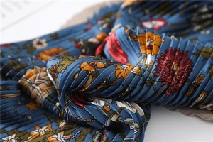 Macro shot of pleated silk scarf with floral and insect prints on deep blue fabric