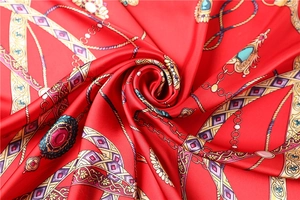 Détail d'un foulard en satin rouge avec chaînes dorées et motifs d'émeraudes