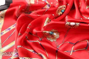 Texture détaillée d'un carré de soie rouge avec chaînes dorées et motifs de bijoux