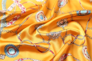 Gros plan d'un foulard en soie jaune avec motifs de bijoux royaux et détails de chaînes