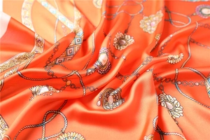 Gros plan d'un foulard en soie orange avec motif de chaînes dorées et bijoux à l'aspect satiné