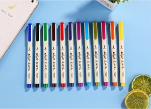 Flat lay of 13 colorful soft-tip pens for calligraphy and drawing on light blue background
