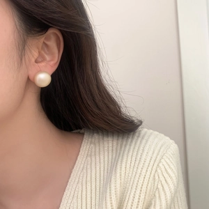 Close-up of elegant oversized cream pearl stud earrings worn by a model in a soft setting