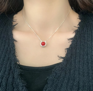 Detail of silver horseshoe necklace with a red bead pendant worn on model