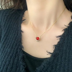 Minimalist gold horseshoe pendant necklace with a red bead on a female model