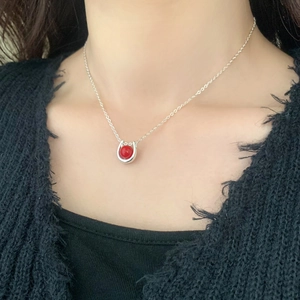 Close-up of a silver U-shaped necklace with a red round gemstone bead on a model