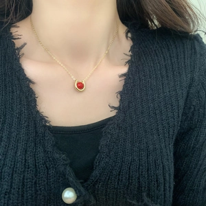 Close-up of minimalist gold necklace with U-shaped pendant and a red bead on a model