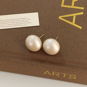Detail of elegant matte pearl stud earrings with gold posts on a vintage fabric display