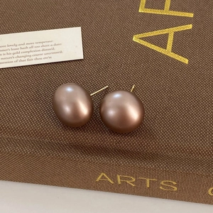 Detail of matte bronze semi-circle stud earrings on a vintage aesthetic background