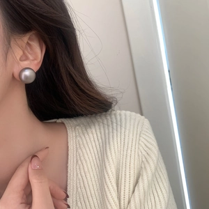 Detail view of a large matte grey pearl stud earring worn on a female model