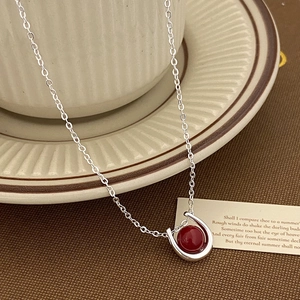 Detail of horseshoe necklace with red gem on beige cup, minimalist silver design