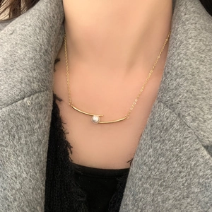 Collier élégant en or avec barre métallique courbée et perle blanche sur un mannequin