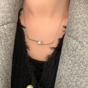 Détail d'un collier de perles minimaliste avec barre métallique courbée sur pull noir