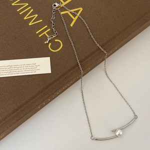 Détail du collier argenté à double arc avec perle ronde posé sur un livre vintage