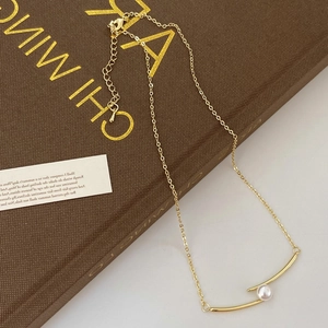 Gros plan d'un collier doré avec pendentif tube incurvé et détail de perle blanche
