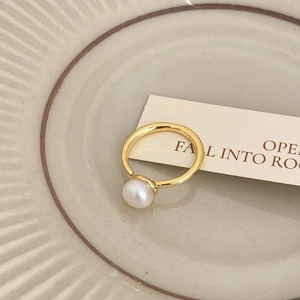 Detailed close-up of a single white pearl set on a minimalist gold ring over ceramic tray