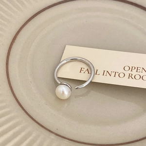 Close-up of minimalist silver open ring with a single white freshwater pearl on ceramic