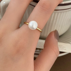 Close-up of an elegant gold ring featuring a single round white pearl on a female finger